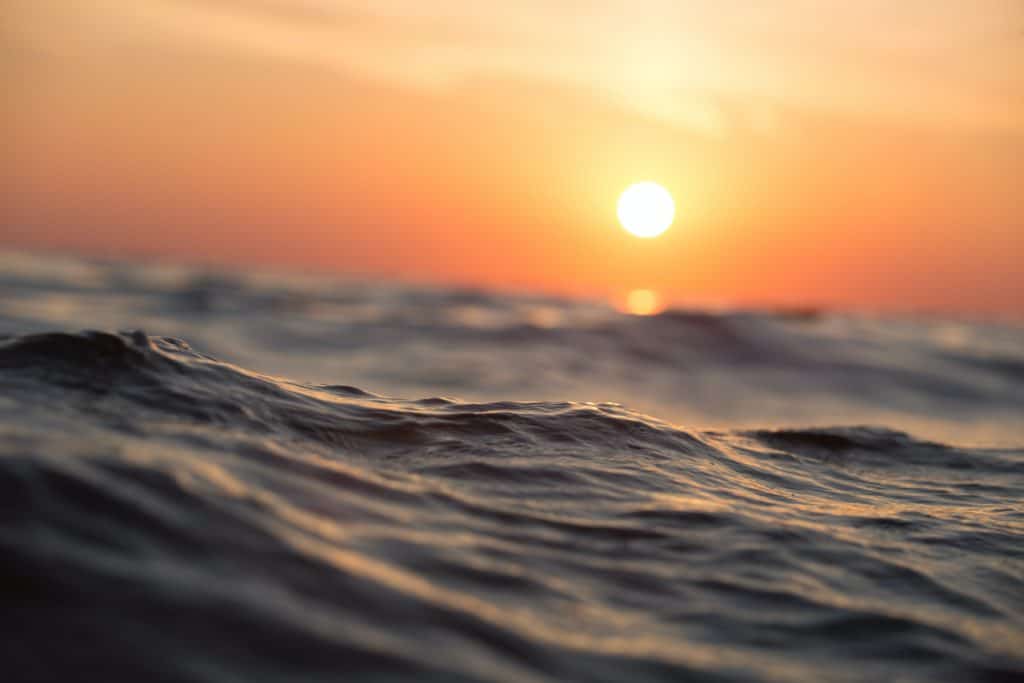 A closeup image of the ocean with the setting sun in the background.