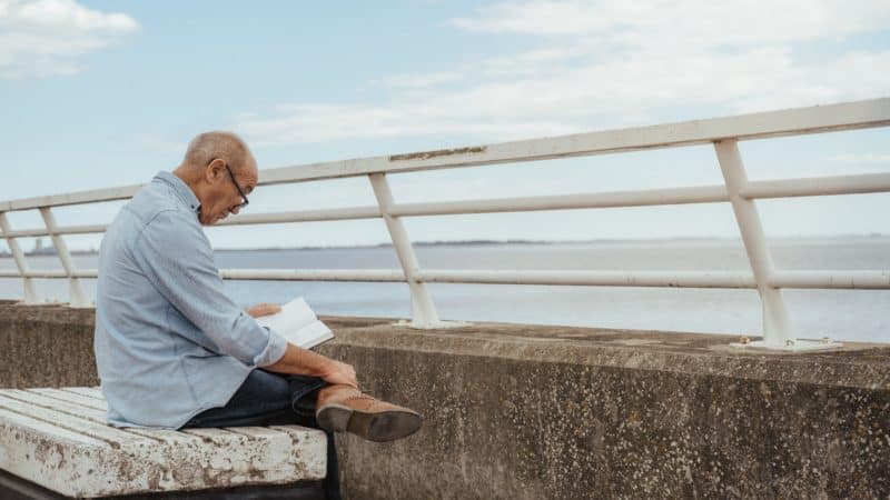 Man reading the Bible on a bench outside 