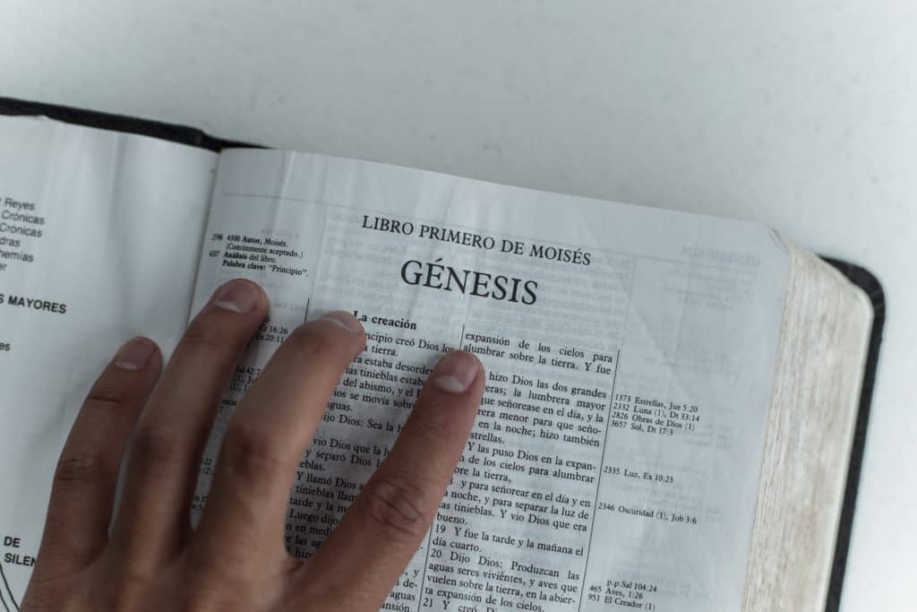 The Bible open with hands placed under the word Genesis