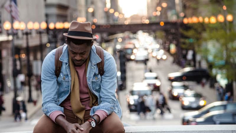 A sad man sitting on a bridge over a busy street.