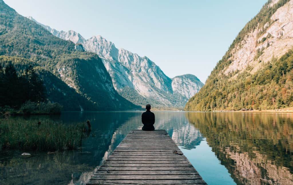 A man sitting on a dock looking at a beautiful mountain landscape.