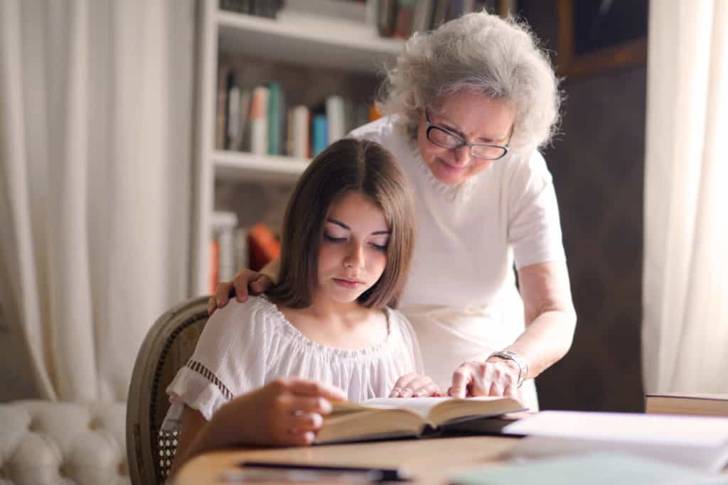 An older woman helping a young girl read the Bible.