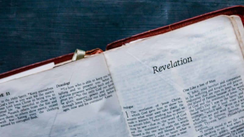 The Bible open to the book of Revelation on a black table as it mentions of many end time prophecies and of Jesus' return