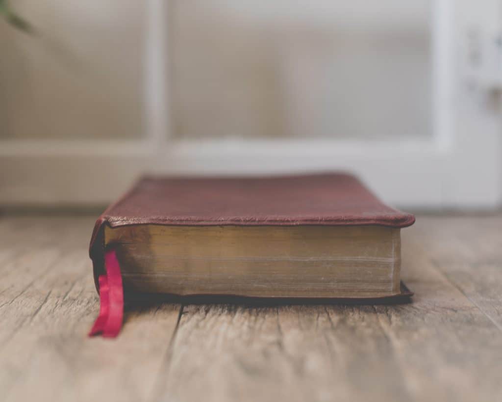 closed brown leather bible sitting on an old wooden floor