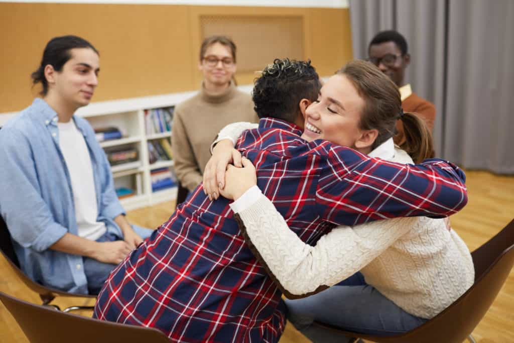 Portrait of two young people hugging in support group meeting.