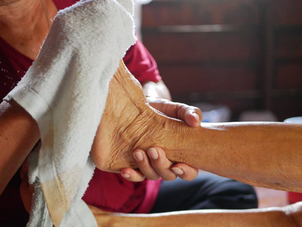 Hands of a woman holding an older person's feet, while gently wiping / cleaning it with a wet washcloth