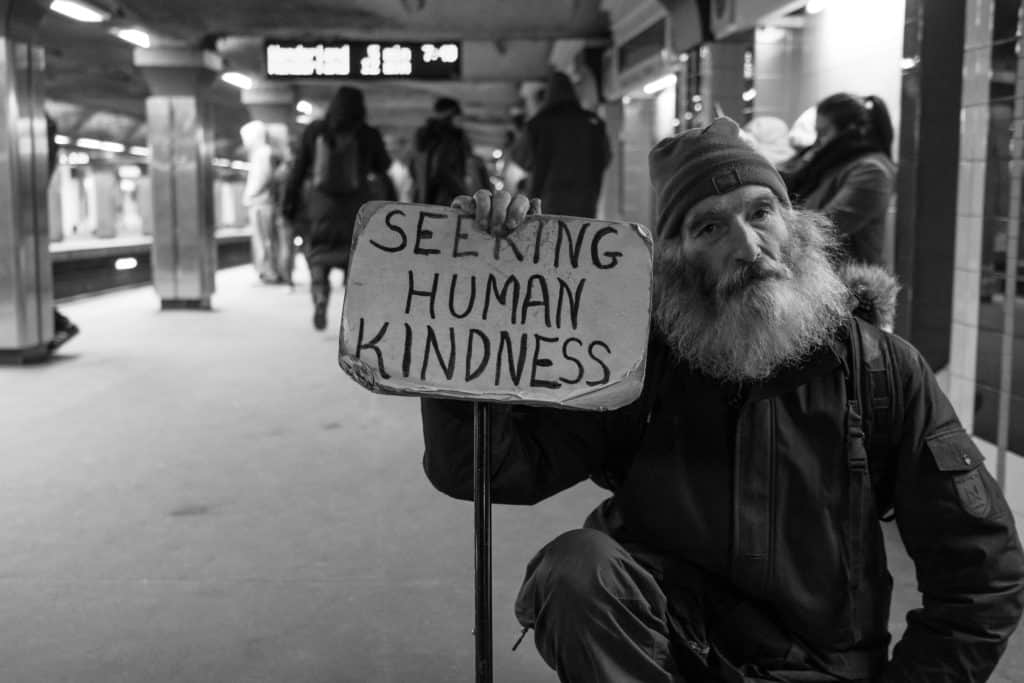 A homeless man holding a sign that says 'seeking human kindness'