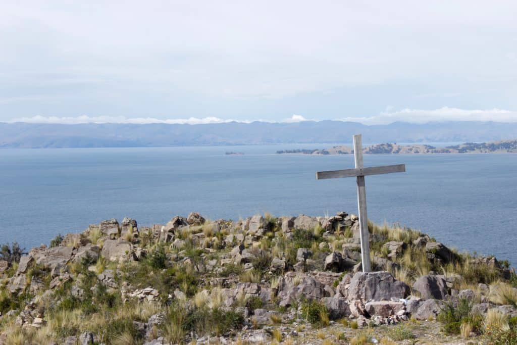 a small wooden cross erected on a rocky mountain with a body of water in the background