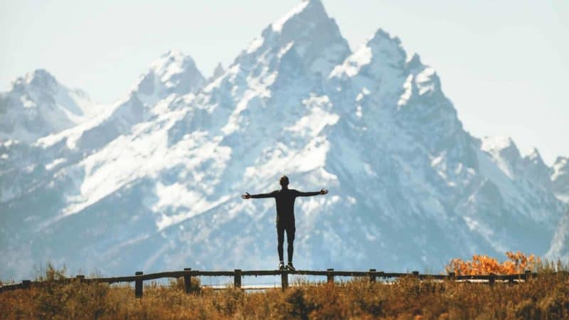 A man looking at a mountain with his arms outstretched as we study about the experience of joy of salvation and victory over sin