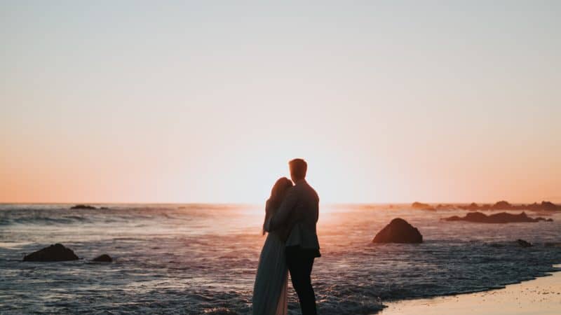 A couple standing on the beach looking at the sunset as God prepares us today to enter into the Millennium