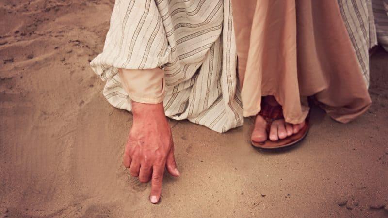 Jesus writing in the sand as the religious leaders bring a woman caught in adulatory to Him