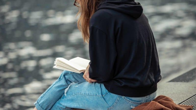 Una mujer joven sentada en un muelle de la lectura como estudiar la Palabra de Dios acerca de los signos de el pronto regreso de Jesús