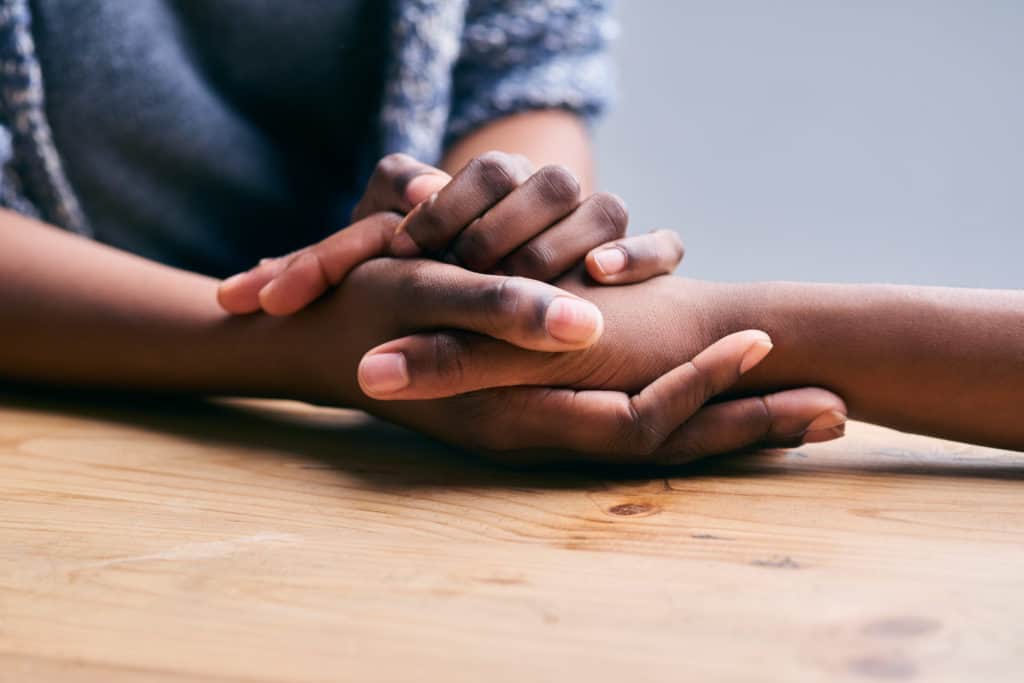 Cropped shot of a two people holding hands in comfort on a table