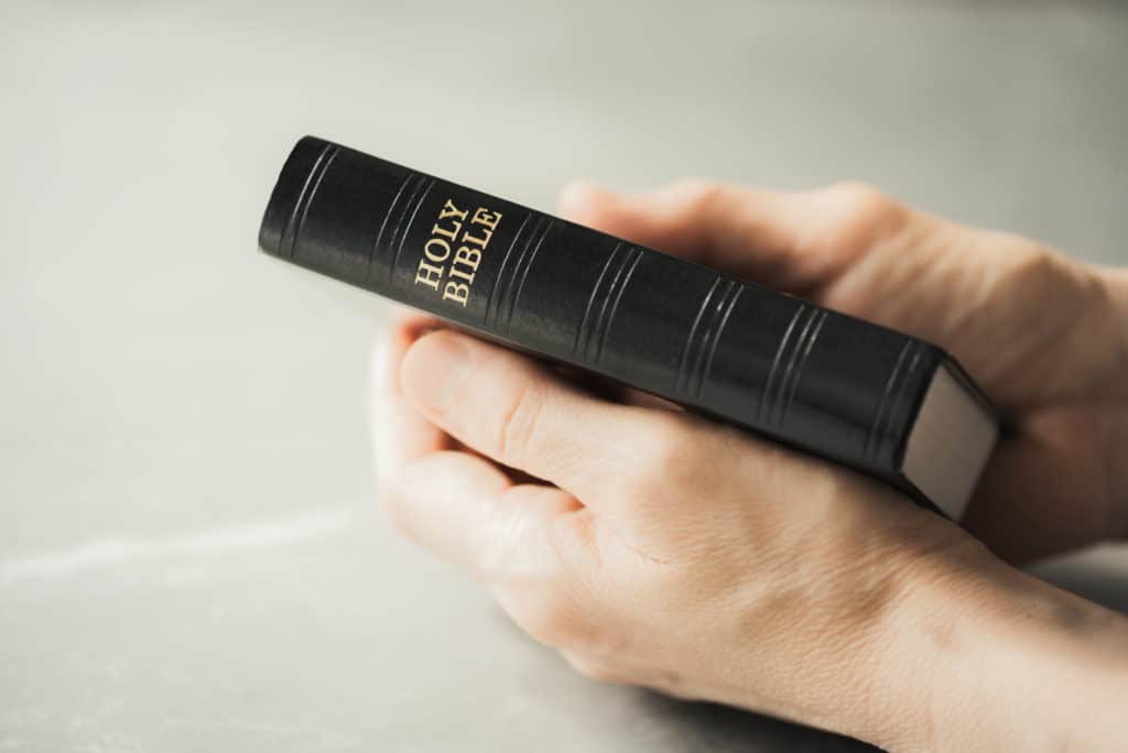 Hands holding Holy Bible over grey background as we learn the importance of the Word of God in the Remnant Church