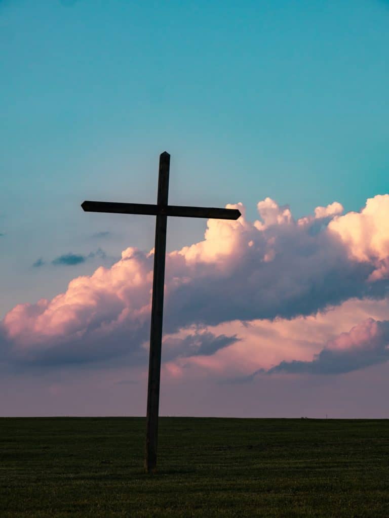 Silhouette of the cross in a field against a cloudy sunset.