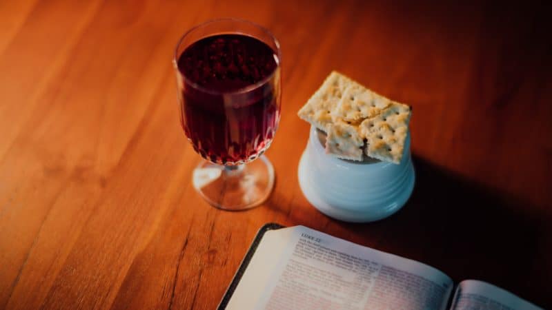 Glass of wine and broken bread next to an open Bible as Jesus gave us the ordinance of the Lord's Supper