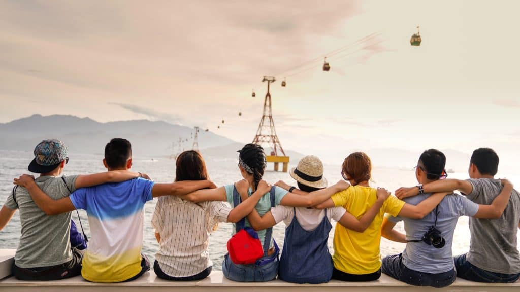 A group of friends sitting by a lake with their arms around each other. 