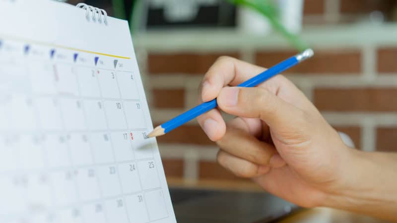 Close-up of a person marking a calendar with a pencil.