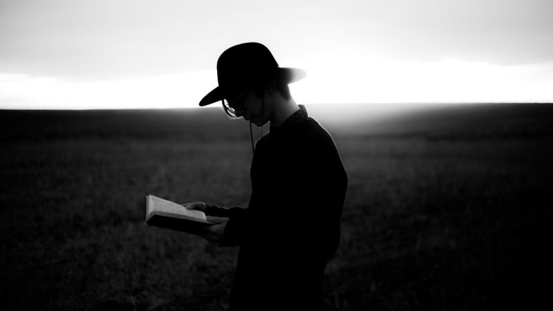 A young man standing in a field reading the Bible.