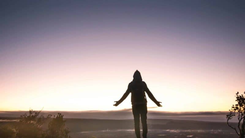 A person standing in the desert at dusk with their arms outstretched.