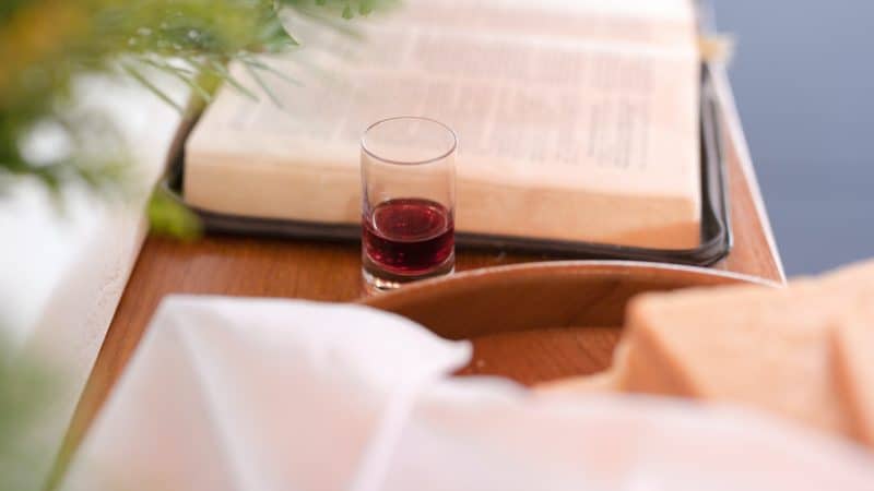 Glass of wine next to an open Bible and bread as we learn the meaning of the Lord's Supper