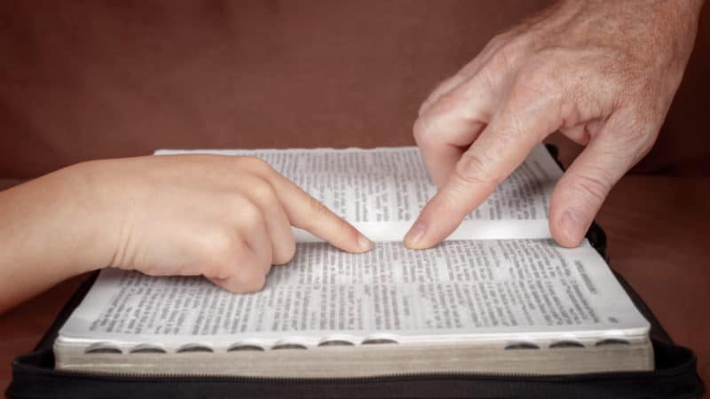 Hand of man pointing something to a child in the Bible book. 