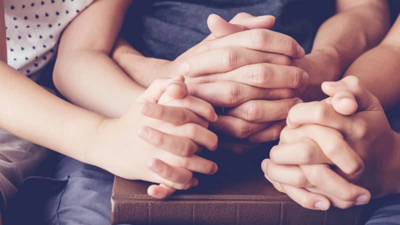 Children praying with parent at home. Closeup of hands on a Bible.