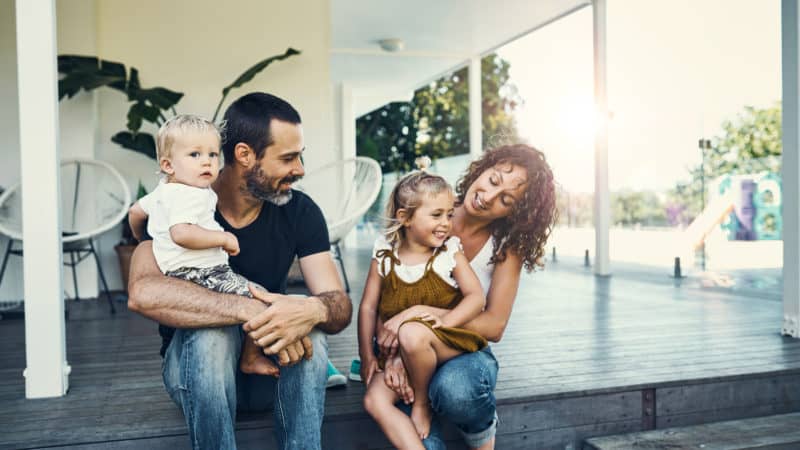 A happy young family sitting on their porch as we study principles of parenting based on Biblical guidance