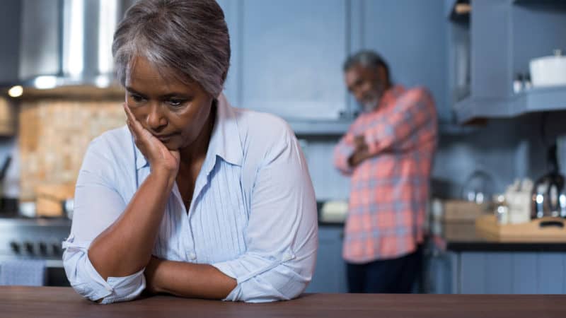 Sad woman with man in background at home as we study Biblical principles to resolve conflicts in marriage