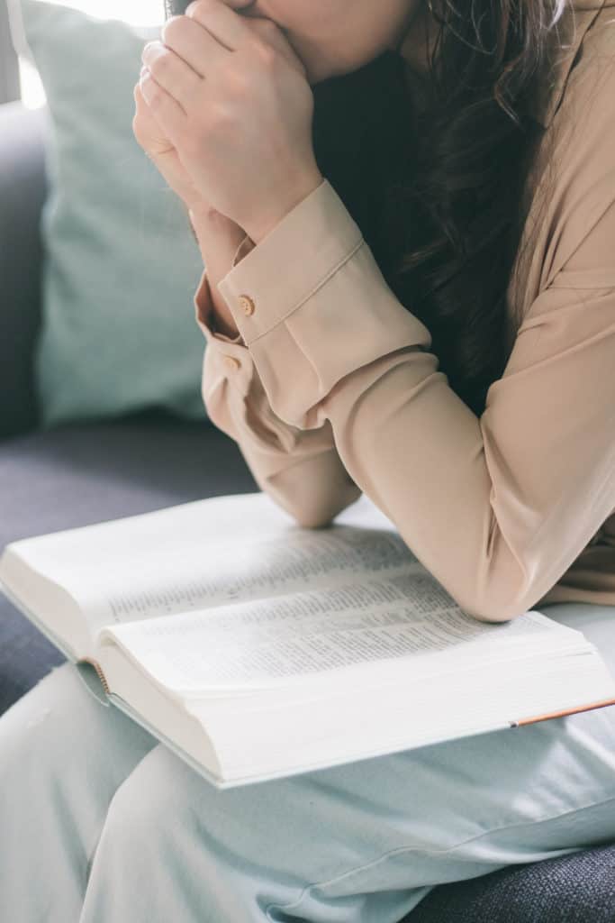 A woman reading the Bible with her hands folded in prayer as we study the importance of submitting our plans to God's will