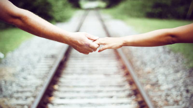 Married couple reaching over a railroad to hold hands as we study in the Bible about the love in marriage