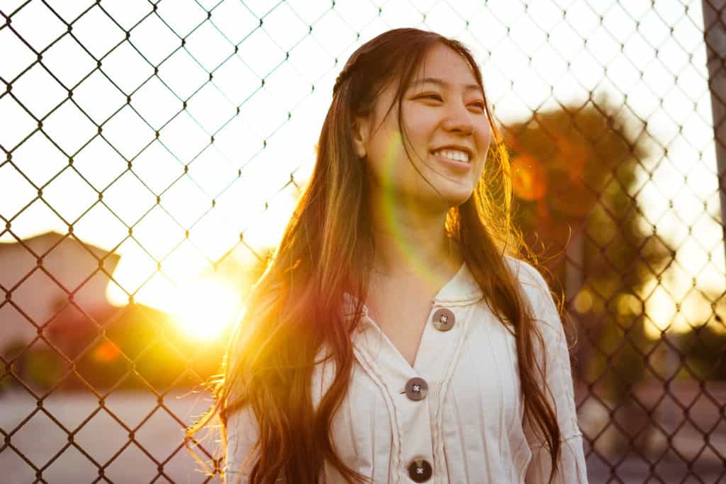 A smiling woman with the sun setting behind her.