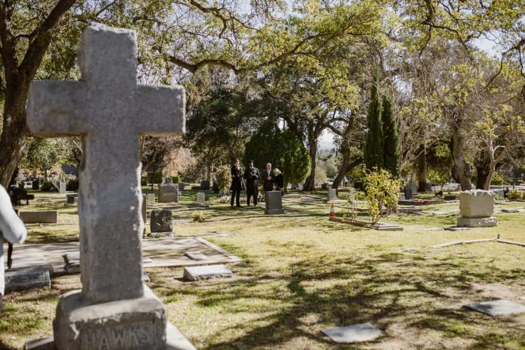 People in a graveyard standing by a grave.