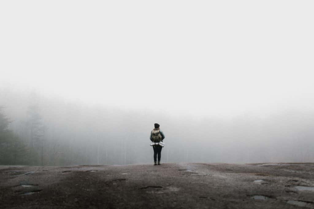 A woman on a hike looking over a foggy forest.