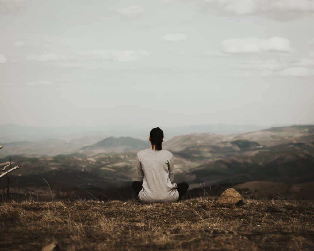 A woman sitting looking out at a hilly landscape.