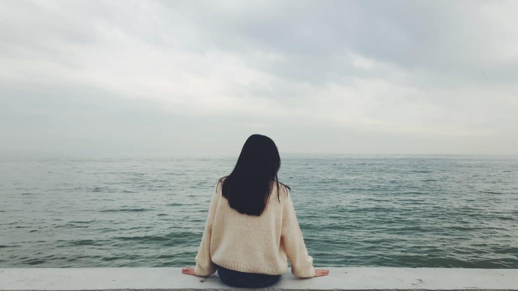 A woman sitting on a short wall looking out over the ocean.