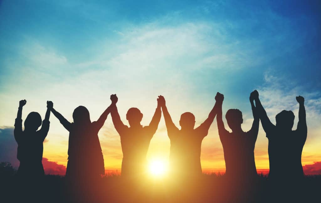 Silhouette of a group holding hands over head in sunset sky evening. 