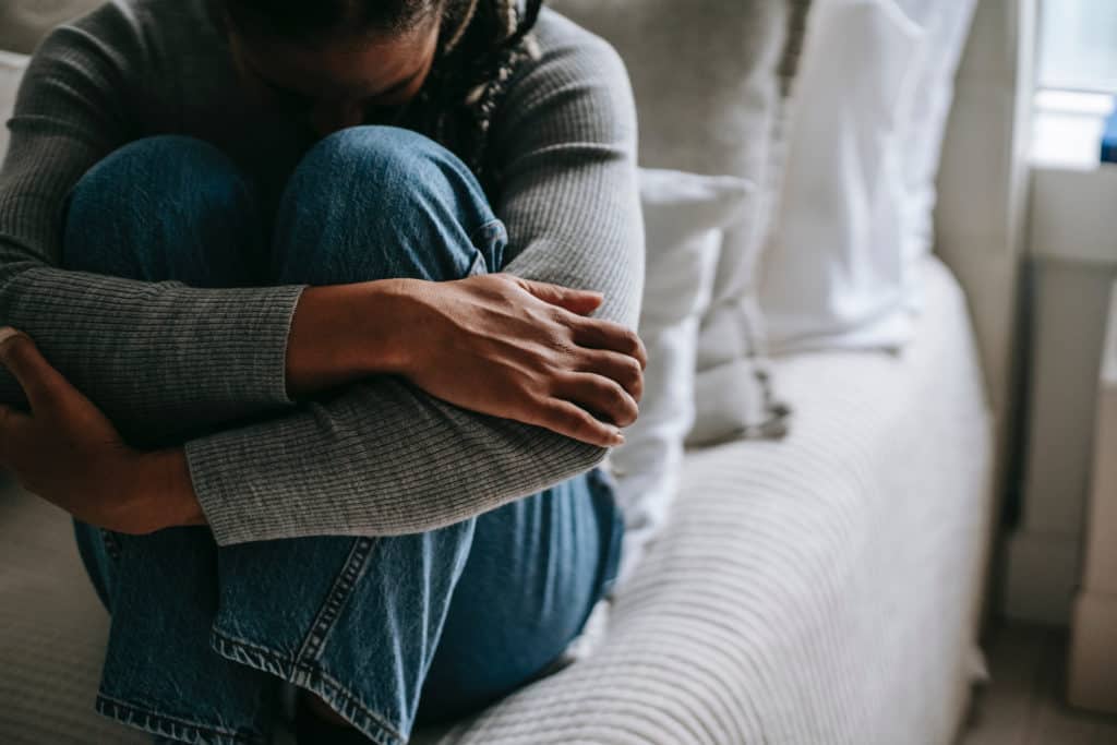 A sad woman crying on her bed with her knees tucked up to her chest.