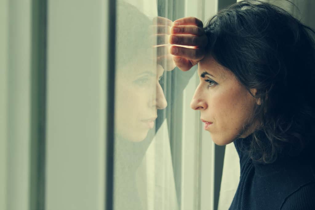 Woman stands in front of the window, looking out.