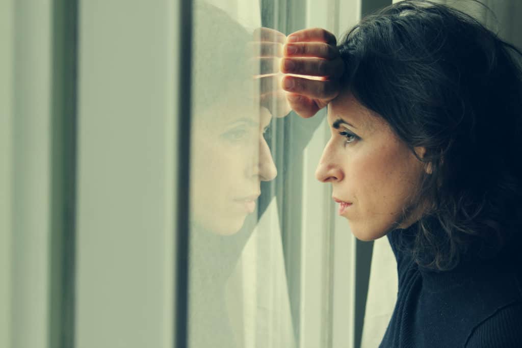 Woman stands in front of the window, looking out. 