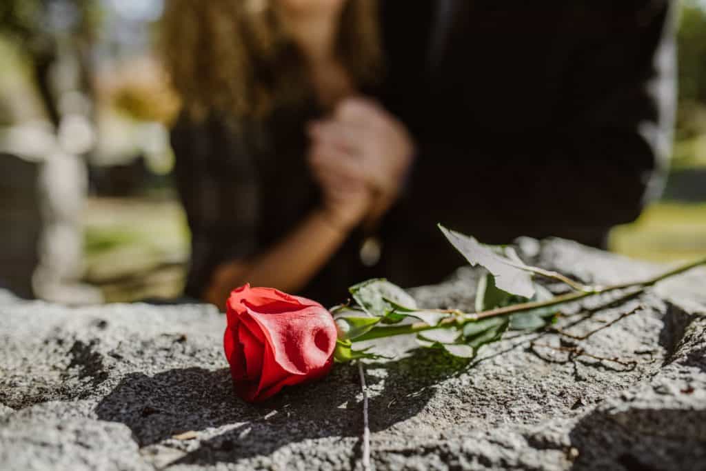 A couple grieving by a grave. A closeup on a rose on top of the headstone.