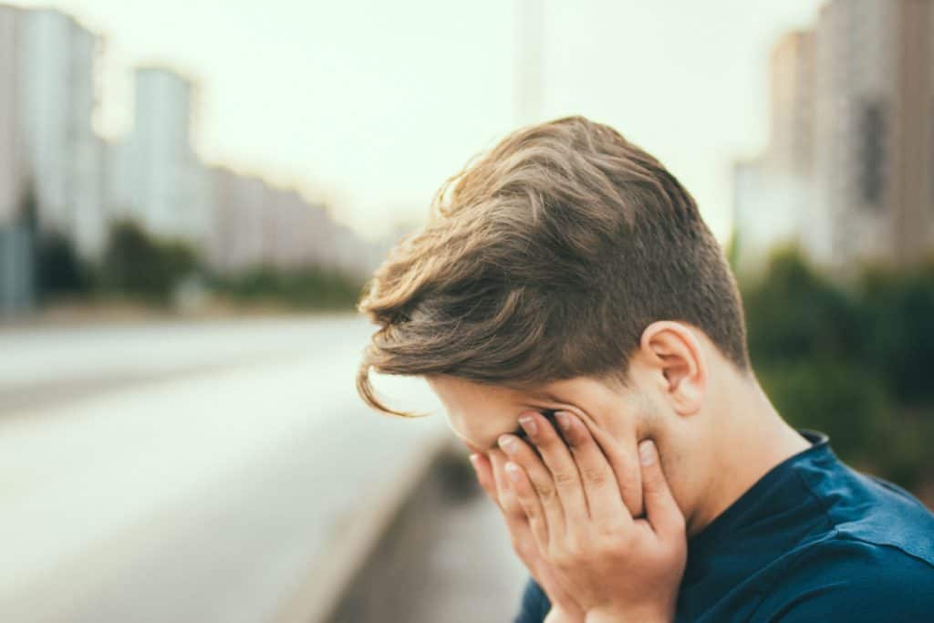 An upset young man covering his eyes.