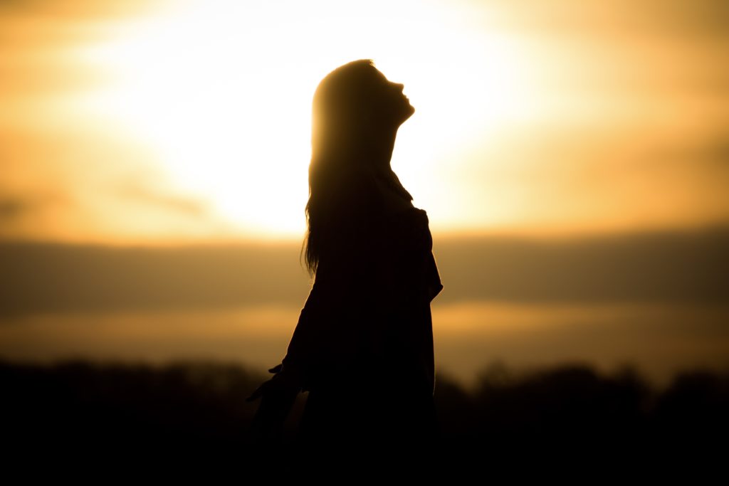 Silhouette of a woman looking up in front of sunset.