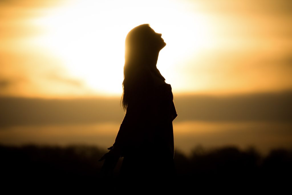 Silhouette of a woman looking up in front of sunset. 