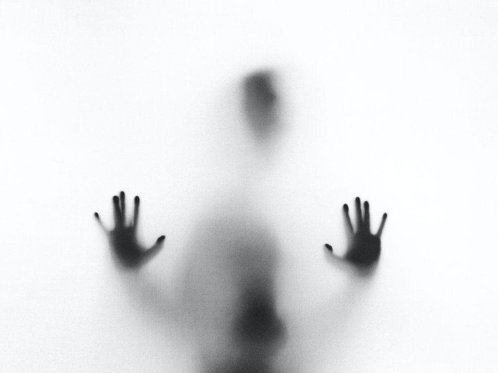 A dark figure on the other side of frosted glass with their hands on the glass. 