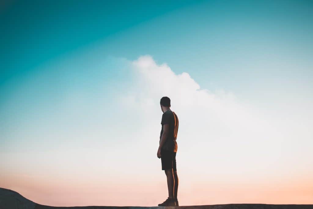 A man standing and looking out at the sky at sunset.