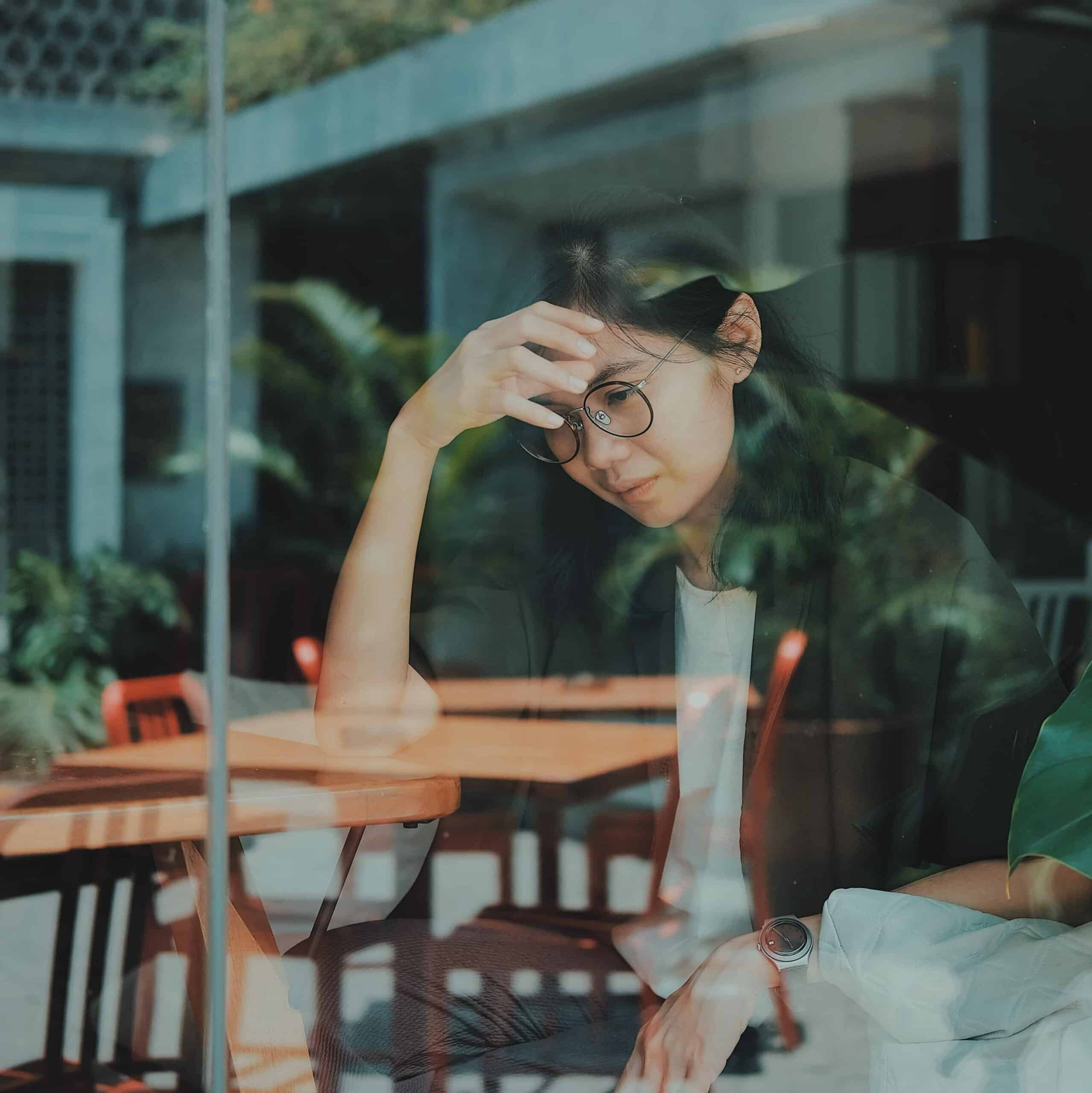 A sad, pensive young woman sitting by a cafe window.