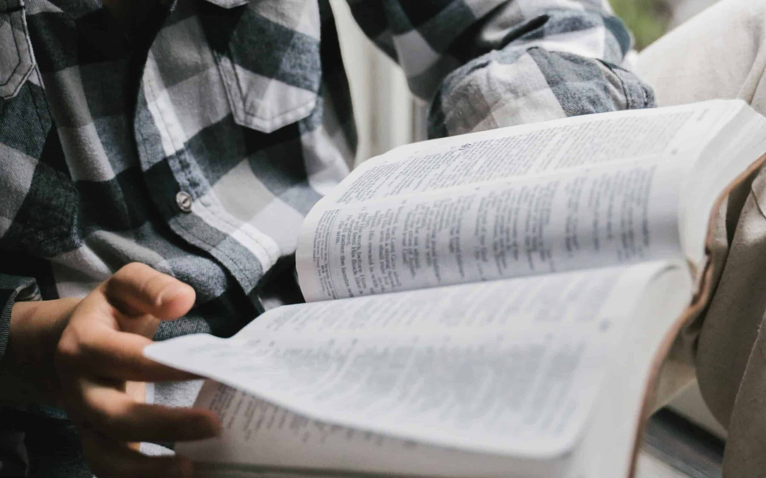 A young woman reading the Bible by a window.