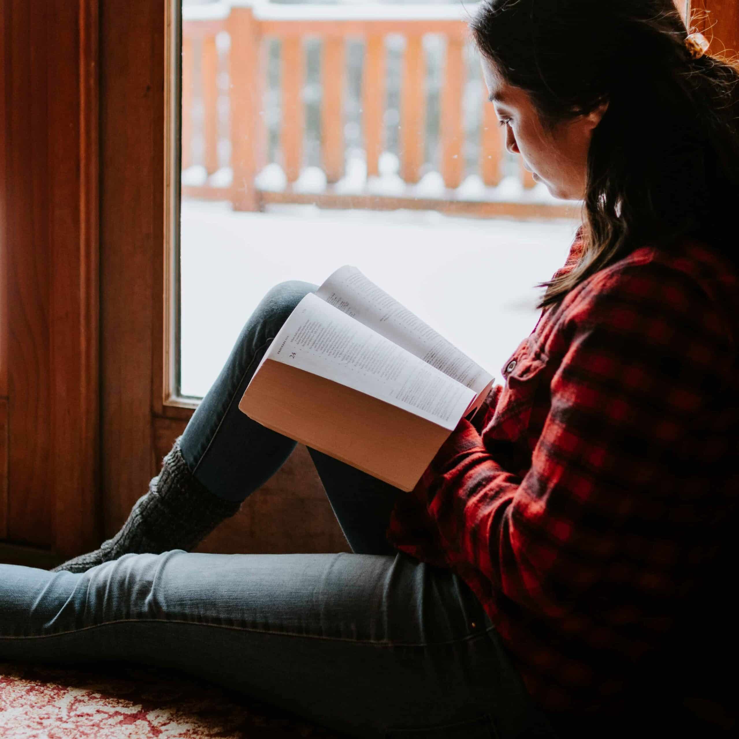 A woman reading the Bible by a window.