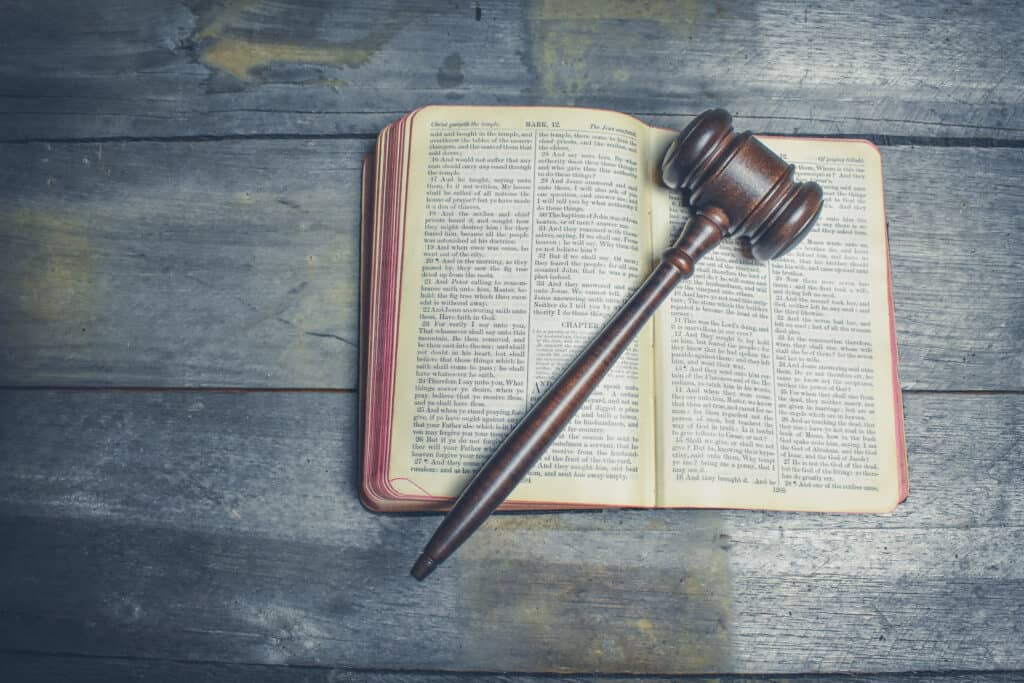 A judges gavel resting on an open Bible laying on a wood grey washed table. 